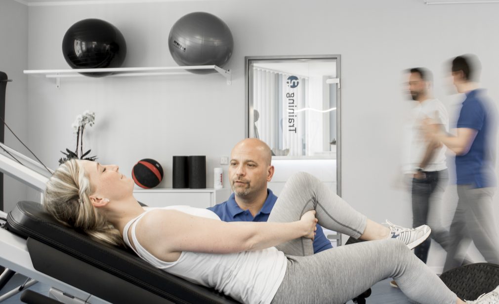 Sportlerin auf Trainingsgerät, Trainer unterstützend daneben