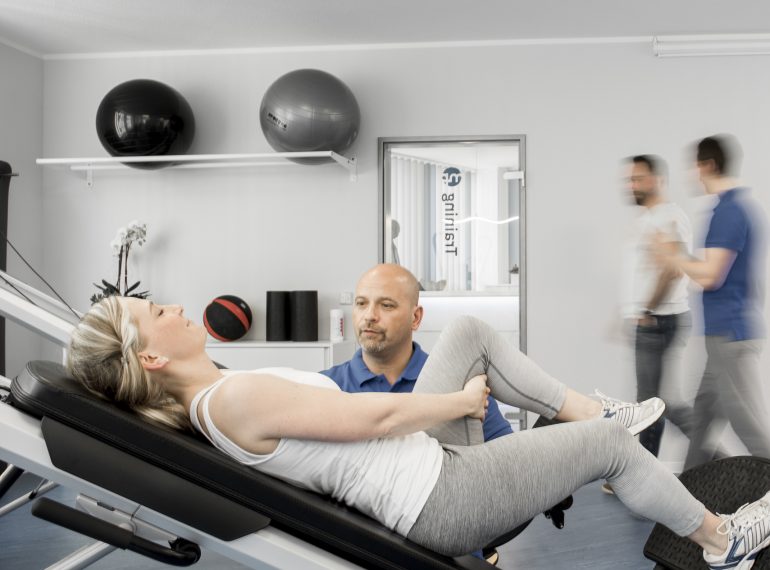 Sportlerin auf Trainingsgerät, Trainer unterstützend daneben