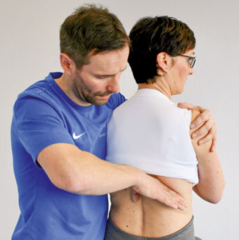 Therapeut stabilisiert den Schultergürtel der sitzenden Patientin und schiebt mit der rechten Hand den Angulus costae nach ventral