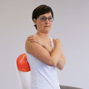 Patientin sitzt mit vor der Brust verschränkten Armen, ein Ball liegt zwischen Stuhllehne und den rechten Kostotransversalgelenken
